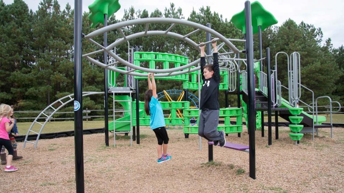 Children hanging from curved overhead bars at Carrollton Elementary School playground, engaging in active play.