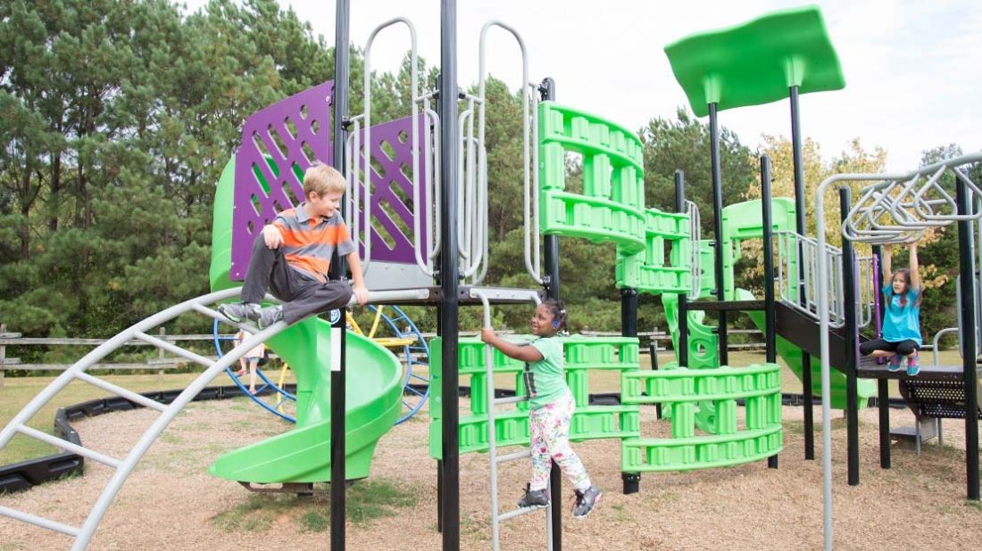 Children playing on climbing structures, ladders, and monkey bars at Carrollton Elementary School playground.
